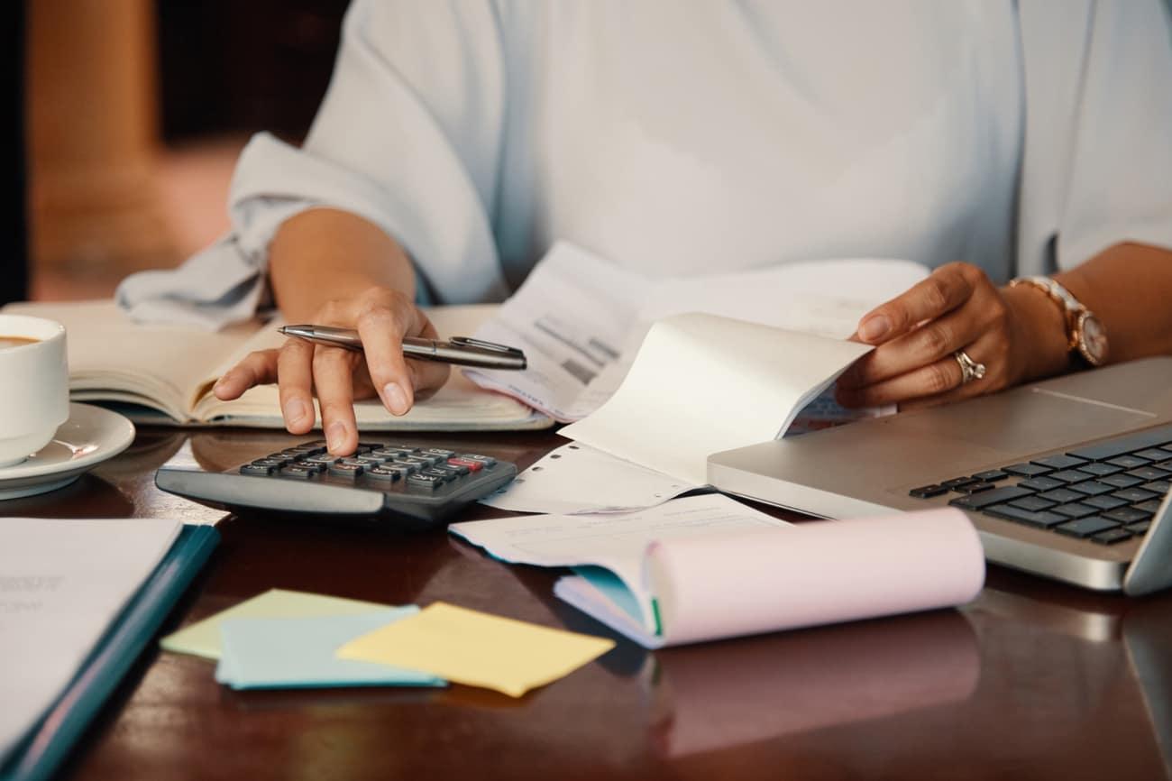 Manos revisando boletas con una calculadora y un computador